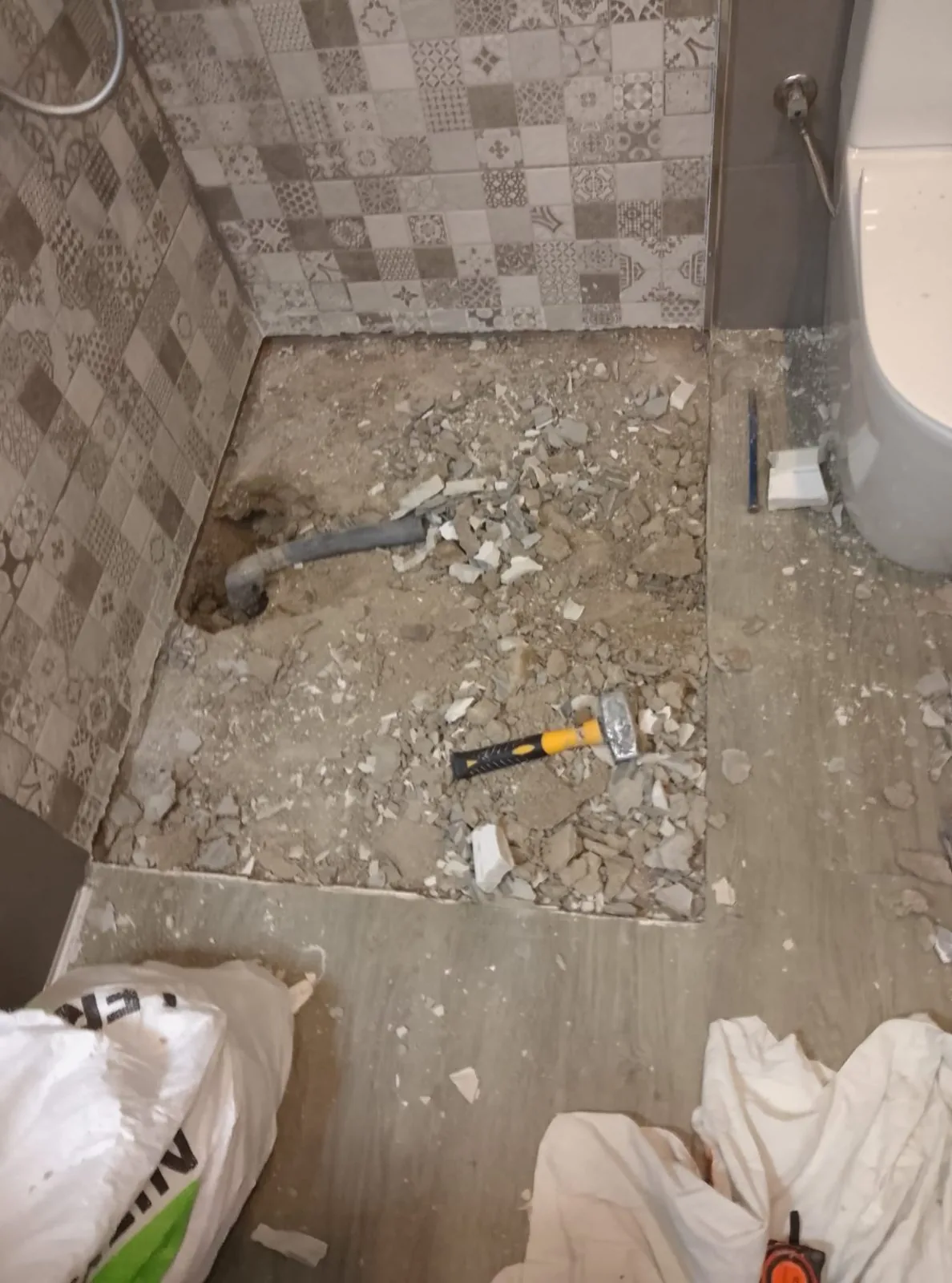 Suelo de ducha demolido con escombros, martillo y desagüe a la vista antes de instalar el plato
