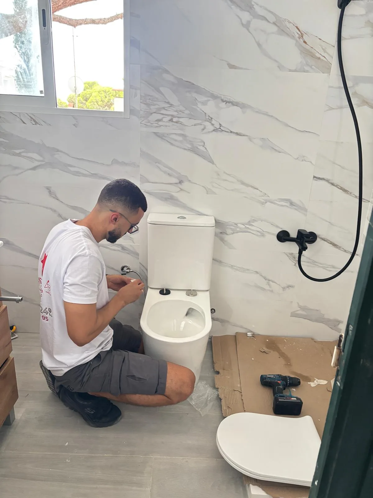 Fontanero instalando un inodoro en un baño con paredes de mármol blanco