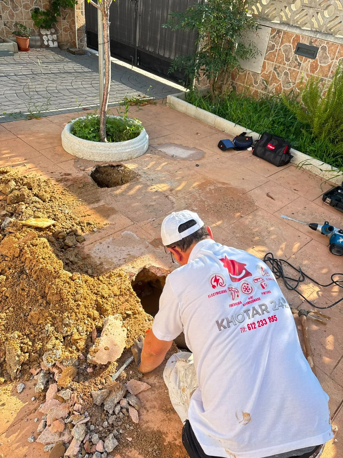 Fontanero arrodillado excavando un registro en el suelo de un patio para acceder a una tubería